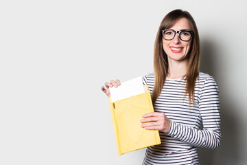 Young woman takes out a letter or notice from a paper envelope on a light background. Concept letter from college, taxes