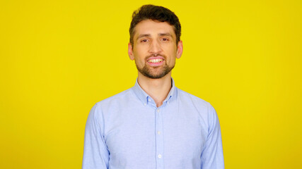 Fototapeta premium Handsome bearded man in a light blue shirt smiles. Businessman looking at the camera on a yellow background with place for text