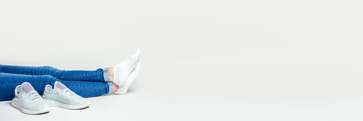 Legs of a woman sitting on the floor on a light background with sneakers. Banner
