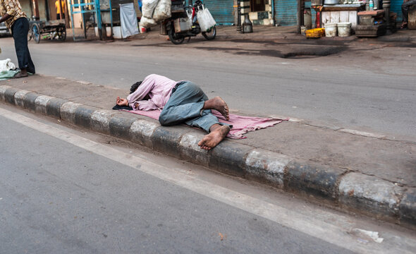 A homeless man sleeping on the street footpath during the day time. A poverty stricken poor person resting on road divider in the morning. Under privileged people living a difficult life on roadside.
