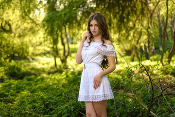 Portrait of a beautiful young girl in light white dress in the summer park