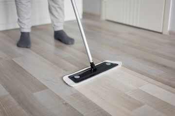 housekeeping concept - man cleaning wooden floor with mop