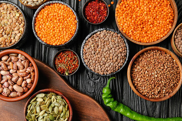 Different raw legumes with spices and buckwheat on table