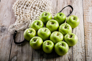 Juicy organic green apples and cotton string mesh bag on a wooden table