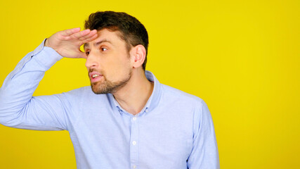 Handsome bearded man looks away with hand to forehead on a yellow background with copyspace. Guy in a light blue shirt. Place for text or product