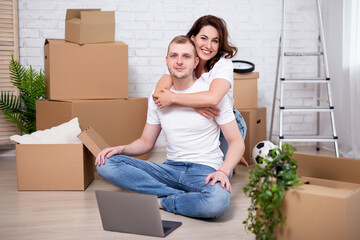 moving day - young couple using laptop in new apartments surrounded with cardboard boxes