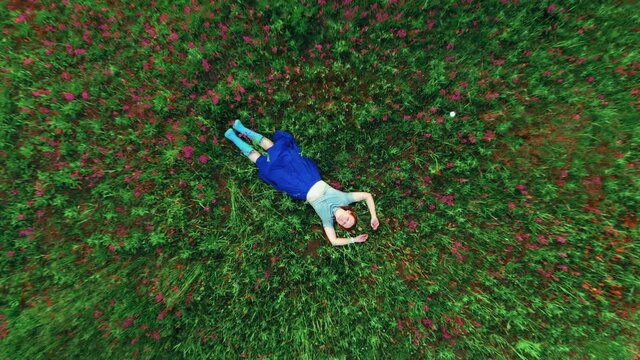 Staycation. 40 years old woman with arms and legs outstretched lying and similing on green grass in park meadow with red flowers. Beautiful summertime. Hello summer, spring and sport consept.