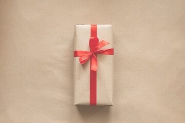 present wrapped in plain recycled paper with red ribbon on beige background