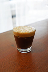 Close up glass of iced black Americano coffee with froth foam served on wooden table