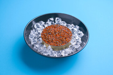 Fototapeta na wymiar Bowl of red caviar on vintage black metal tray with ice over bright blue background. Top view, copy space, flat lay.