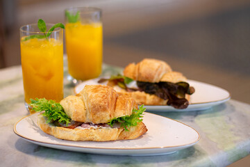 Fresh baked croissant sandwiches with ham and lettuce next to fruit lemonade on marble table