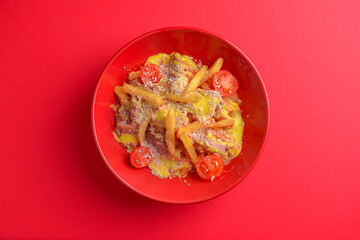 Melting cheddar cheese over the top of french fries covered in spicy sauce with meat and tomatoes. Red background.