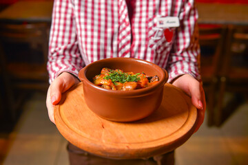 Traditional hot goulash soup. Waiter serving vegetable stew in a pot. Concept for a tasty meal....