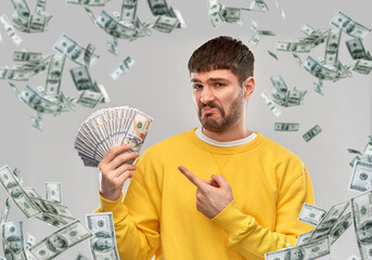 people concept - displeased young man in yellow sweatshirt with dollar money over grey background