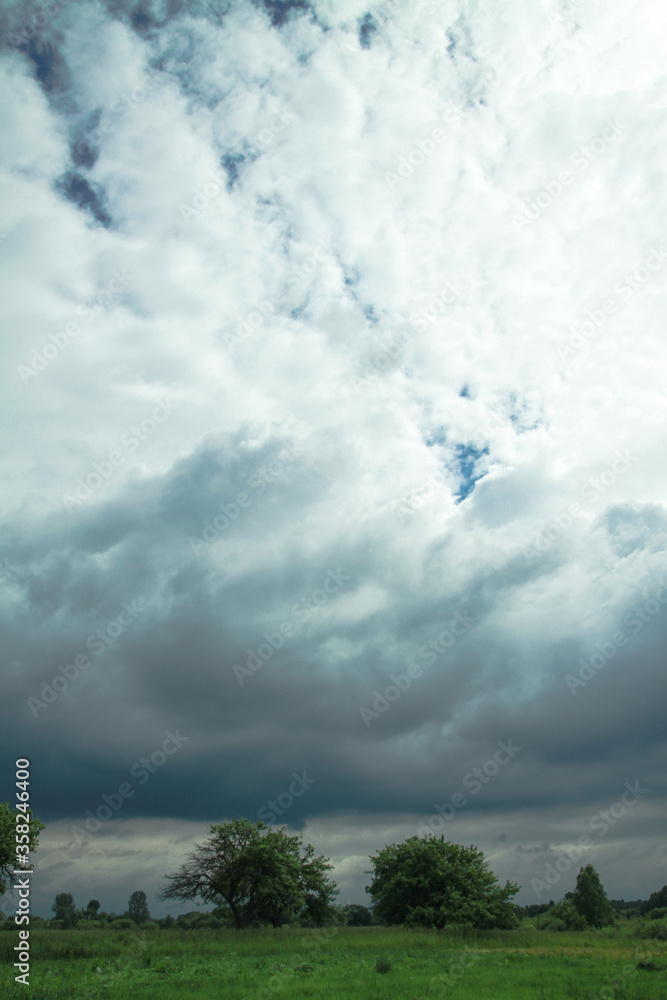 Wall mural thunderous epic clouds in a field near the old garden. stock photo background with heaven.
