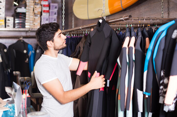 Fototapeta premium portrait of adult male surfer choosing suit for surfing in the store