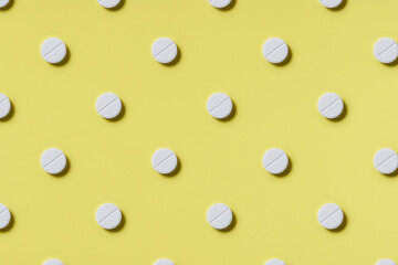 Pattern of white rouned shaped pills on a yellow background. Hard light. Paper background