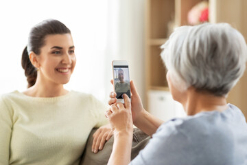 family, generation and people concept - senior mother with smartphone photographing happy smiling adult daughter at home