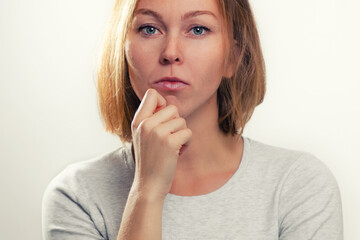 The concept of psychology and emotions. A young blonde woman leans her cheek on her hand, and looks thoughtfully. White background and close up