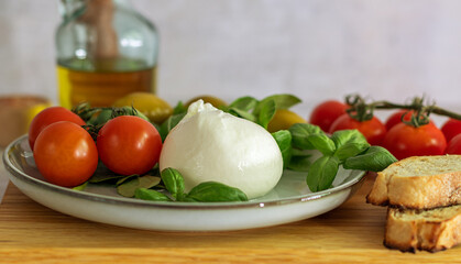Fresh Italian burrata cheese with tomato on a light plate with basil and olives. Close up. Selective focus