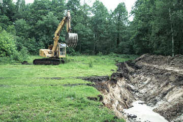 An excavator digs a large trench for building a house. A tractor digs a large lake that is already gaining water. Stock background for design