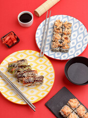 Sushi rolls on colored plates on a red background. A look from above.