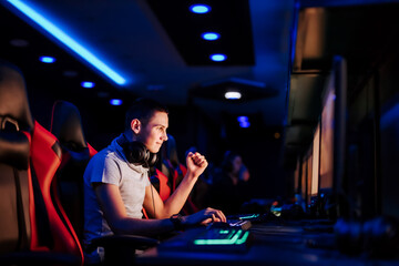 Cheerful young gamer gesturing while playing online video game at cybercafe, portrait, side view. © bnenin