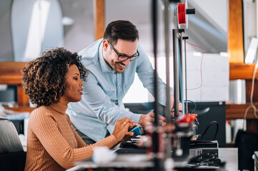 Engineer showing to a young woman how to use 3D printer.