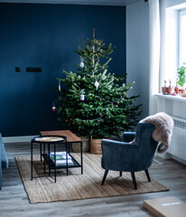 Christmas tree in the interior. Scandinavian style, minimalism. Dark blue wall, grey chair, braided baskets. White paper origami toys.