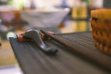 Close-up of wooden spoon and chopsticks next to a rattan rice bowl, inside is a traditional...