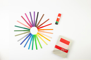 circle made of felt-tip pens with a white background, a glue stick and a ruler on a book