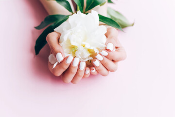 Female hands with white manicure hold a peony.