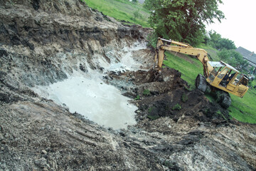 An excavator digs a large trench for building a house. A tractor digs a large lake that is already gaining water. Stock background for design