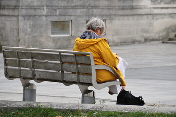 eine ältere Frau  - Rentnerin sitzt allein und einsam auf einer Bank - obrazy, fototapety, plakaty