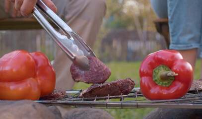 Hand putting piece of meat on barbecue grill outdoor