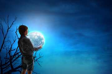Naklejka premium Boy holding moon at night