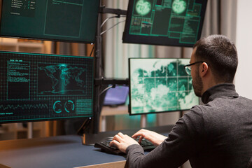 Young hacker with glasses writing a dangerous virus on computer with multiple screens.