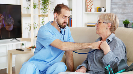 Male doctor putting his stethoscope on and listening old woman heartbeat in nursing home