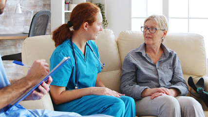 Obraz premium Male assistant writing rehabilitation treatment for senior woman while female doctor is talking with her