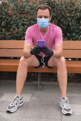 Sportsman with medical mask and gloves, smartphone and earbuds working out, jogging in urban surroundings.