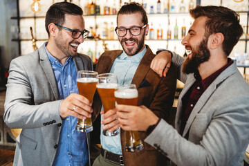 Happy young businessmen drinking beer and talking at pub after work