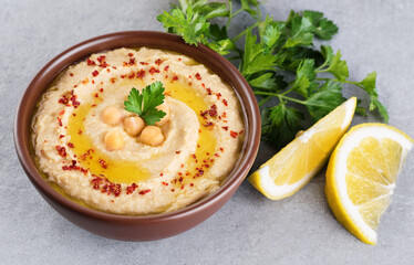 Chickpeas hummus with olive oil, paprika, parsley and lemon on a gray background.
