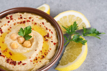 Chickpeas hummus with olive oil, paprika, parsley and lemon on a gray background.