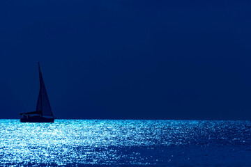 Silhouette of a sailing boat on open sea with moonlight twinkling water.