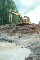 Fototapeta premium An excavator digs a large trench for building a house. A tractor digs a large lake that is already gaining water. Stock background for design
