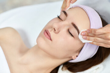 Fototapeta na wymiar beautician cleanses female skin with cotton pad. Perfect cleaning, spa treatment skincare face.