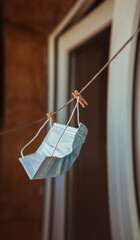A white medical protective mask hanging is dried on the balcony next to the washed laundry.