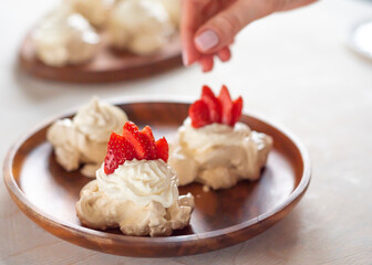 the process of creating Pavlova dessert, decorating the meringue with strawberries