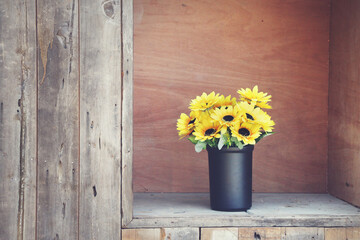 yellow flower In a black pot On a wooden floor.