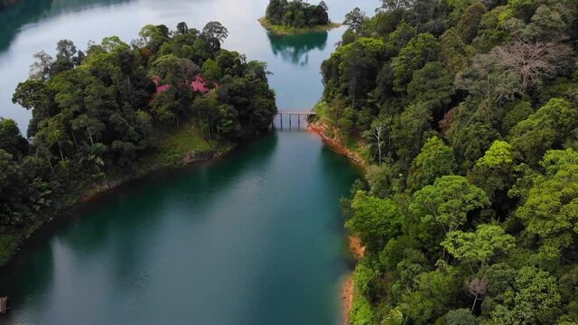 Drone flight over Kenyir Lake in Malaysia. Pan Up from rainforest jungle lagoon setting revealing giant lake scene with mountains in the background. Bright blue water and Lush green forests.